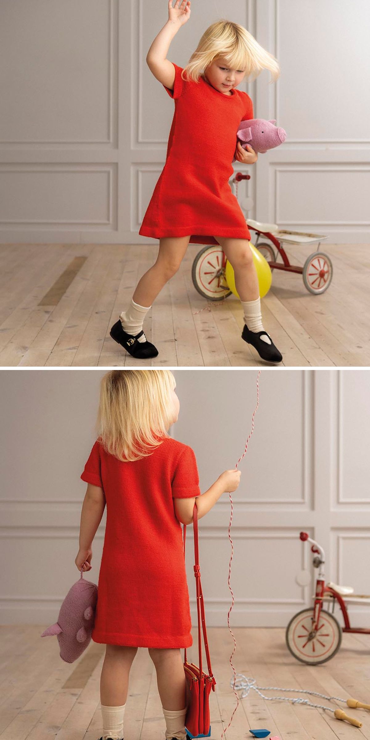 A young child wearing a red knitted dress for baby girl, beige socks, and black shoes holds a stuffed toy and balloon, standing near a tricycle in a room with wooden floors and light-colored walls.