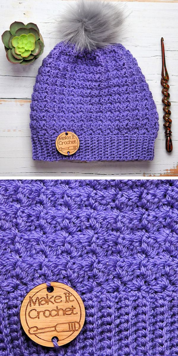A trendy purple crochet beanie with a wooden tag and pom pom.