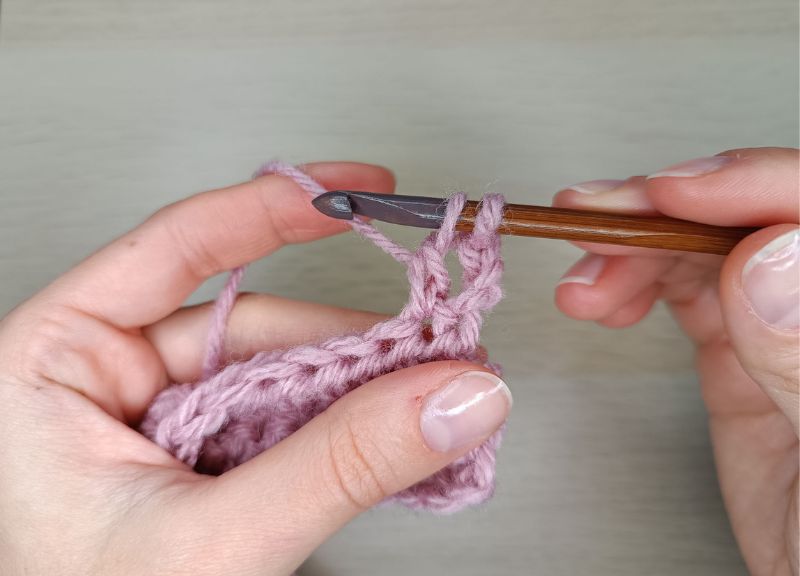 woman's hand holding a crochet hook and pink yarn and mastering double crochet stitch