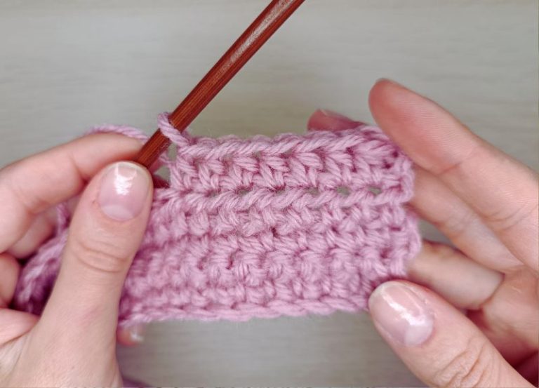 A piece of crocheted fabric in hands presenting half double crochet stitch