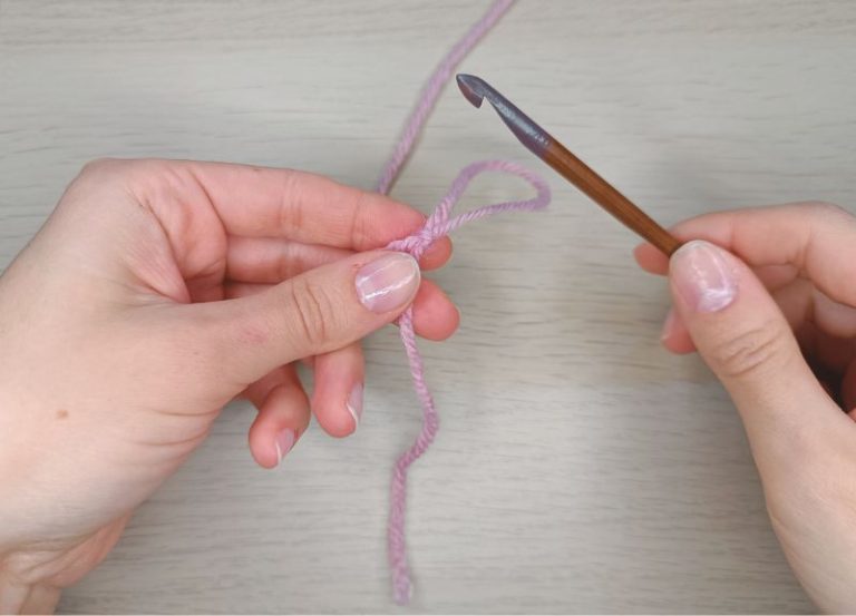 Hands holding a crochet hook and yarn, demonstrating making the slip knot - the beginning of a crochet stitch.