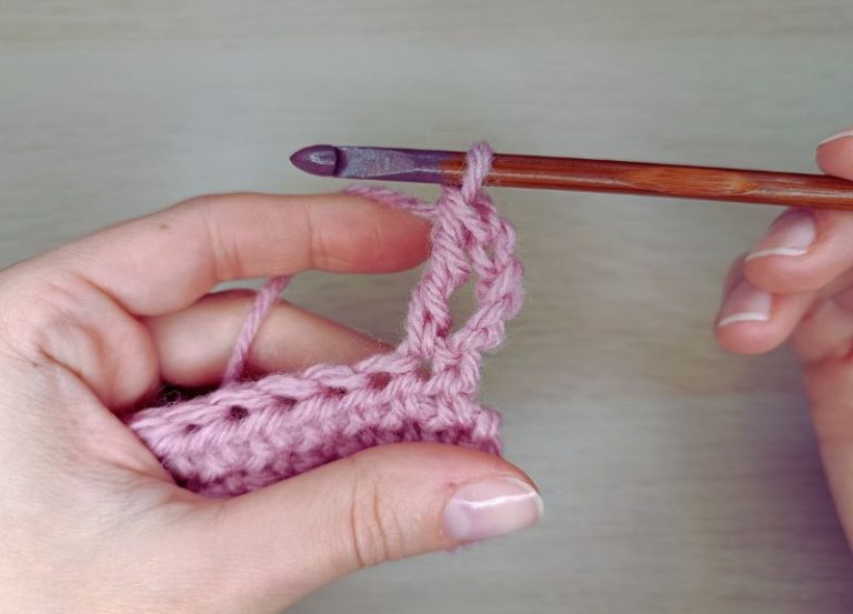 hands holding a crochet hook and some pink fabric showing how to double treble crochet