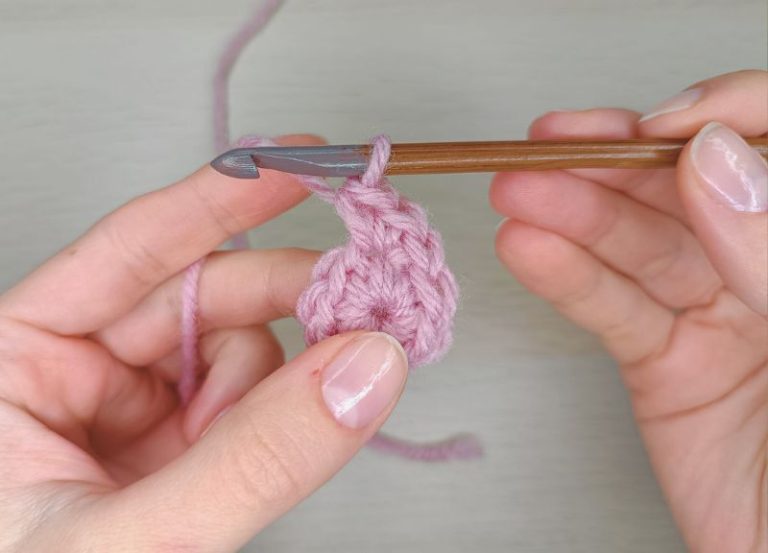 hands holding a crochet hook and a pink yarn demonstrating how to make a magic ring in crochet