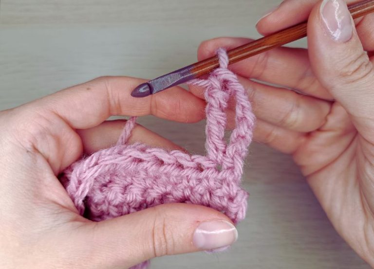 woman's hands holding a crochet hook and some pink fabric demonstrating how to triple treble crochet