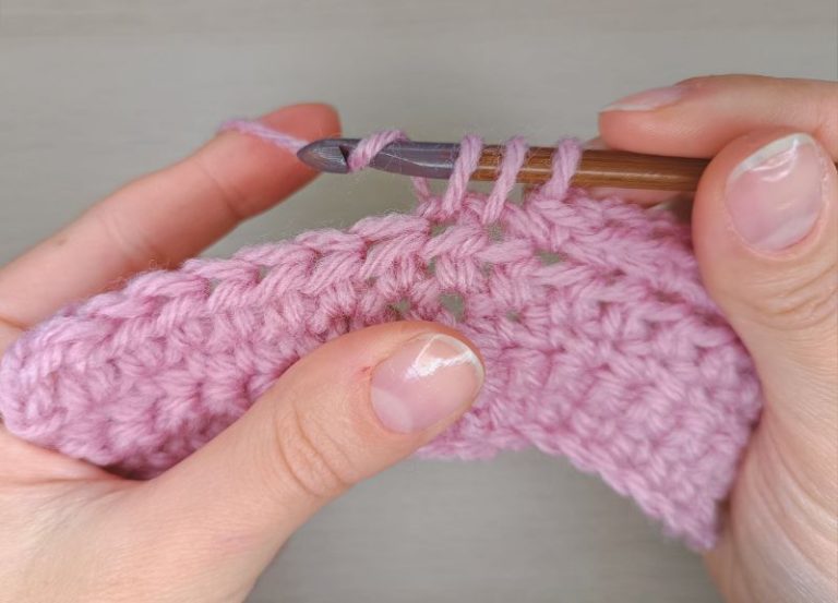 woman's hands holding a piece of pink fabric and a crochet hook and demonstrating how to decrease in crochet