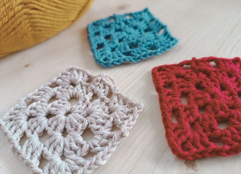 Three crochet granny squares in white, blue and red colors laying on the table