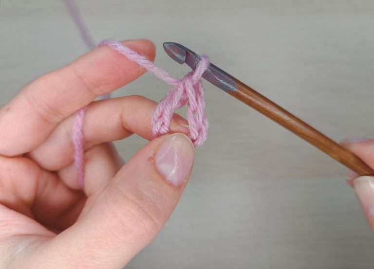 woman's hands with a crochet hook and pink yarn demonstration how to slip stitch crochet