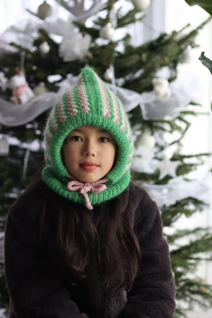 a child wearing knitted hood with pointy top and tie closure under the chin