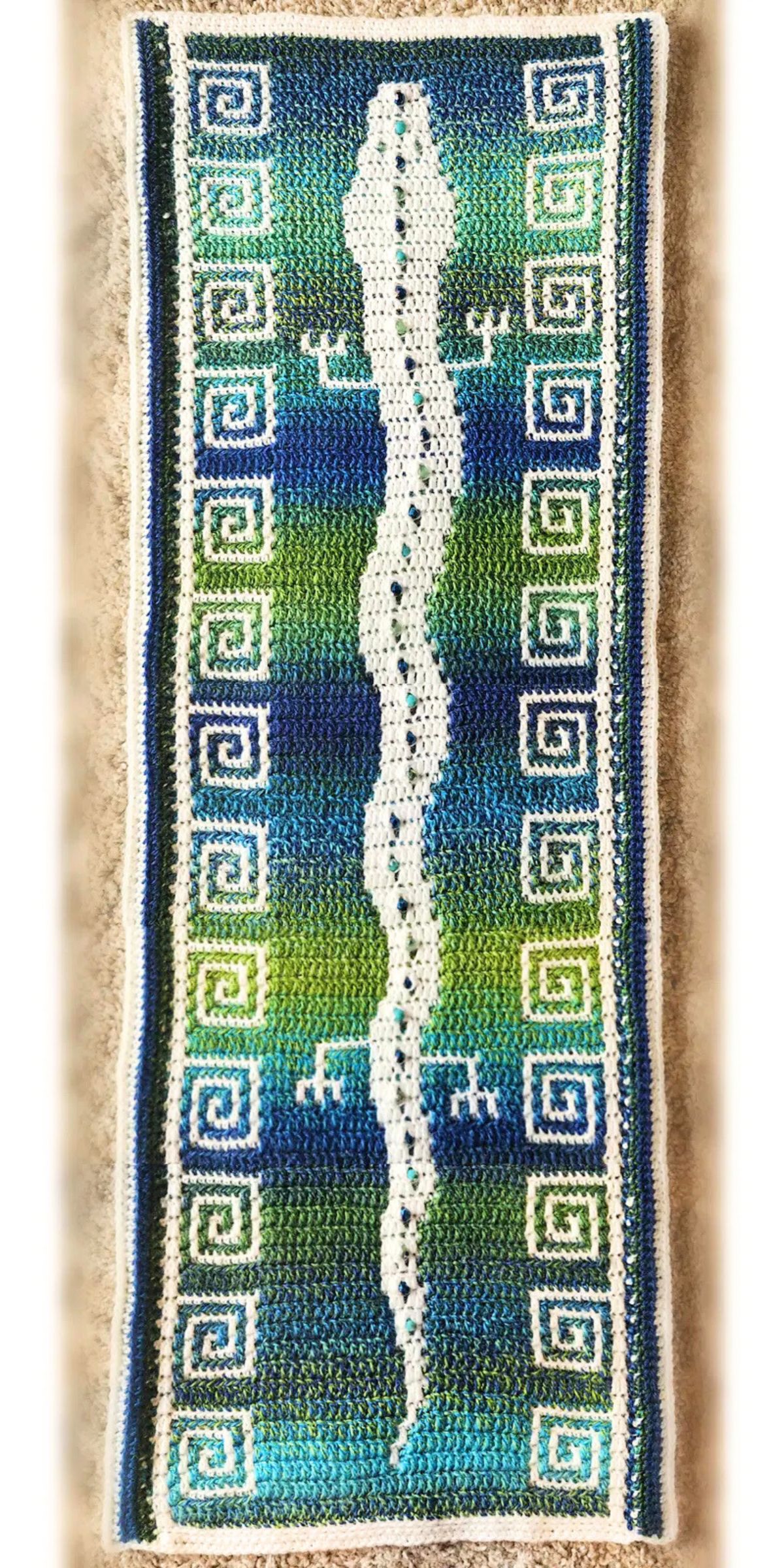 a long crochet wall hanging featuring a colorful mosaic design with a lizard motif running across the middle 
