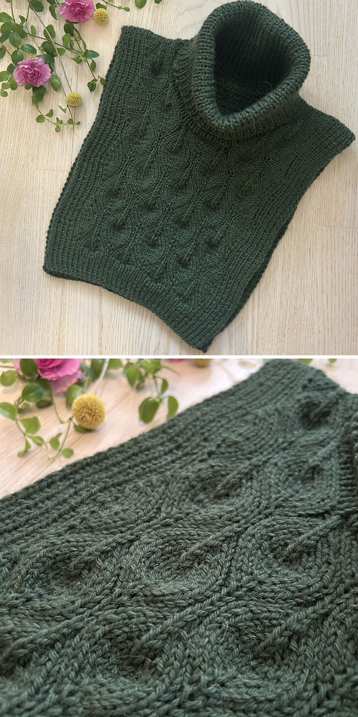 A dark green knitted cowl with a raised cable pattern is displayed on a wooden surface beside pink and yellow flowers. This elegant knitted cowl adds a cozy touch to any outfit.