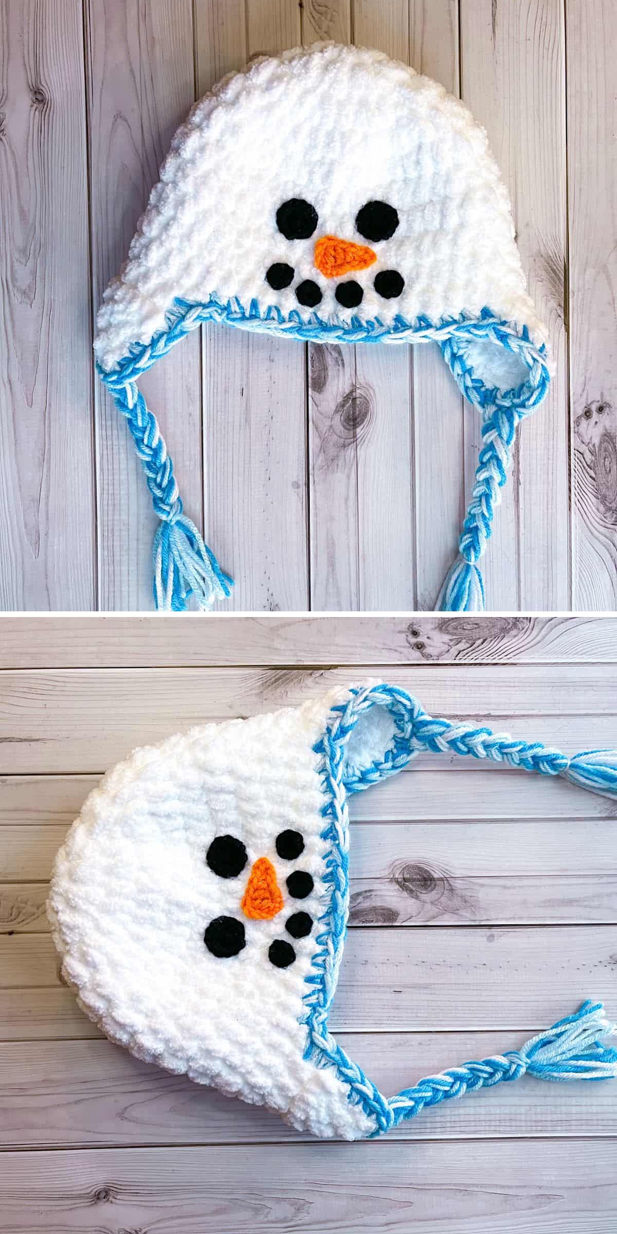 A Crochet Christmas Hat in white with blue trim, braided ties, and a snowman face featuring a carrot nose and black buttons, displayed on a wooden surface.
