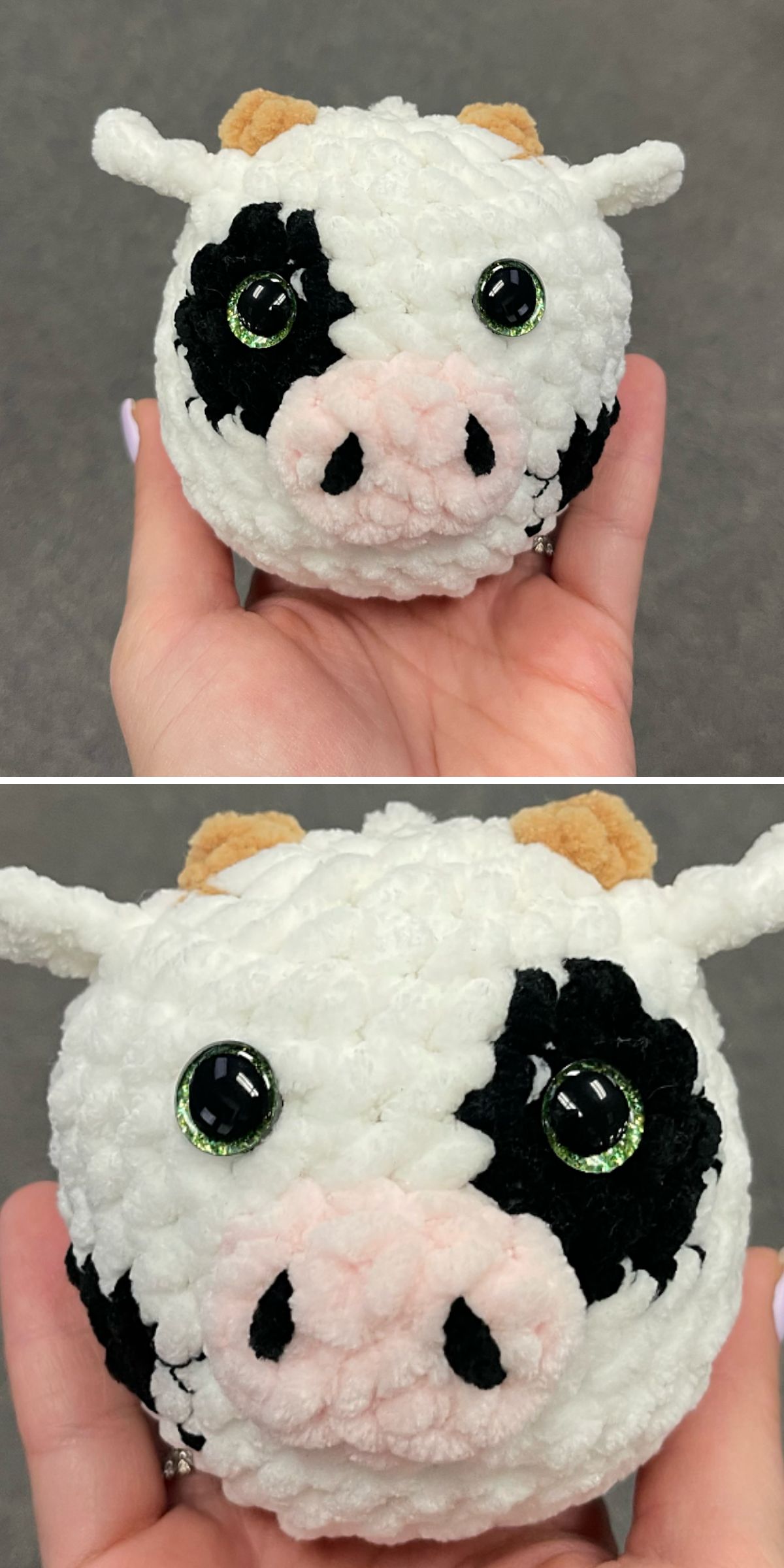 A hand holds a small, round crochet cow plush toy, featuring black spots, large green eyes, beige horns, and pink nostrils.