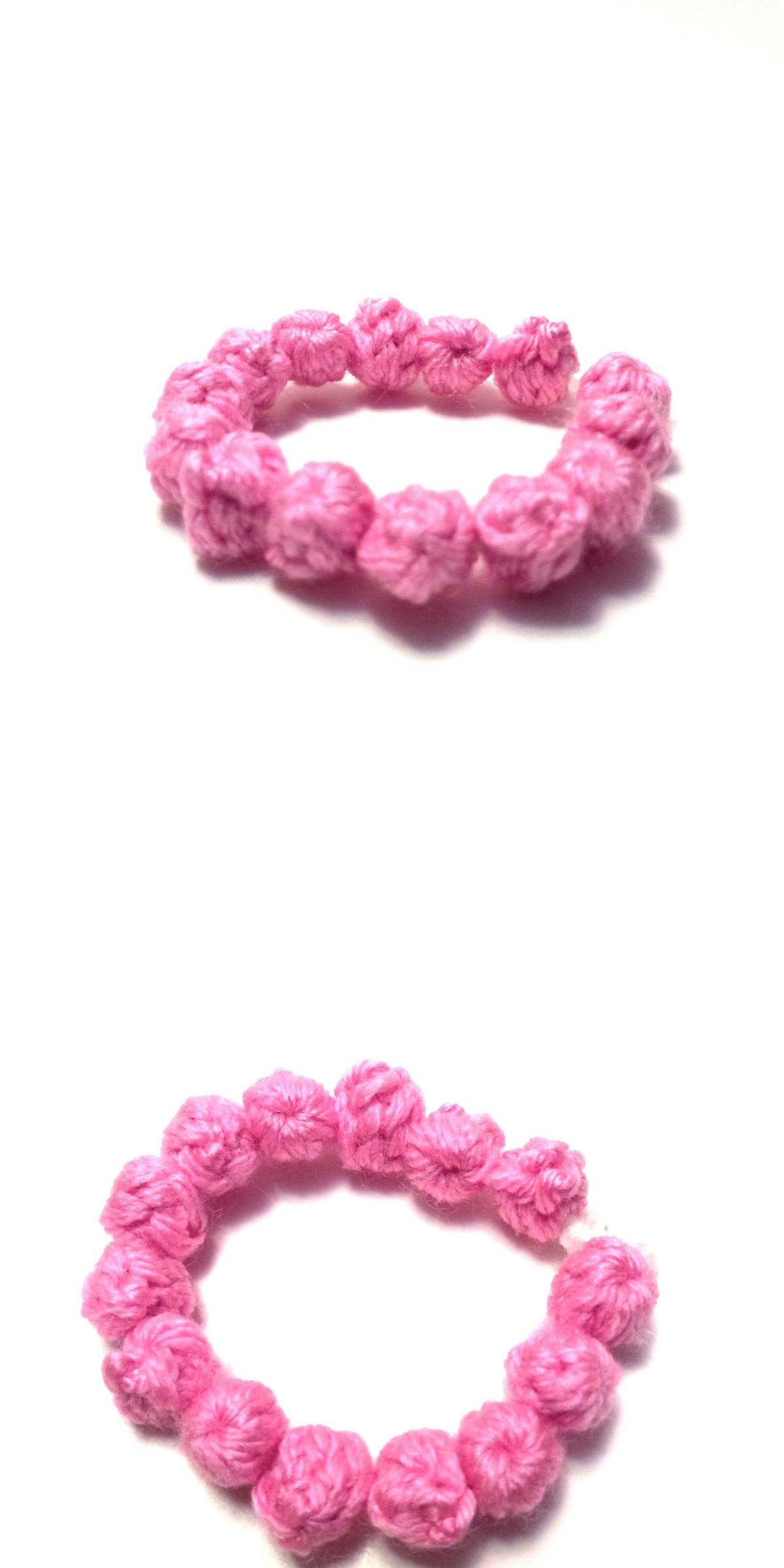 Two pink crochet bracelets, crafted as rings from yarn and featuring small knotted loops, are displayed on a white background.