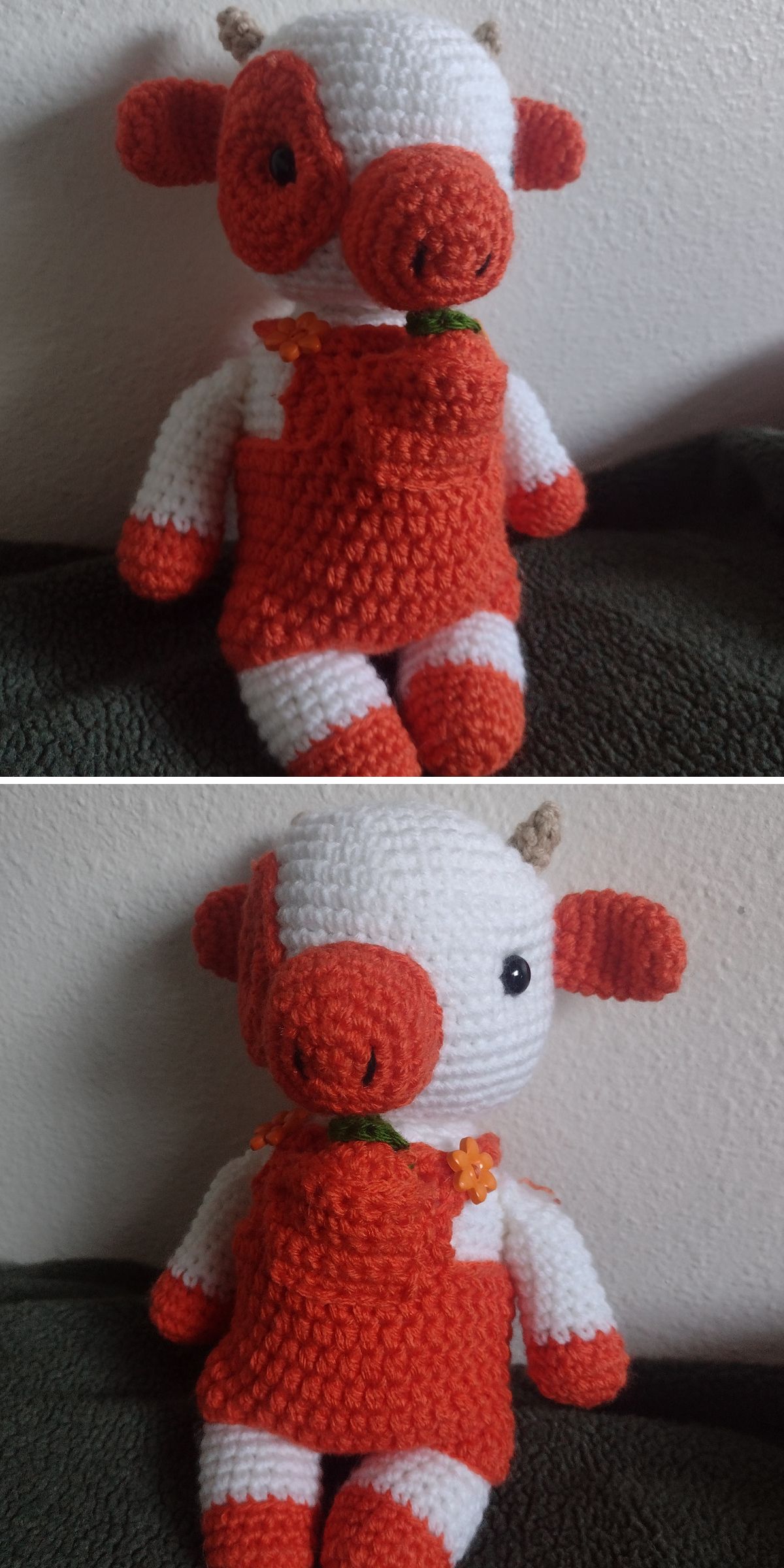 A crochet cow plush toy with orange and white coloring, orange overalls, a green collar, and small brown horns sits against a textured wall.