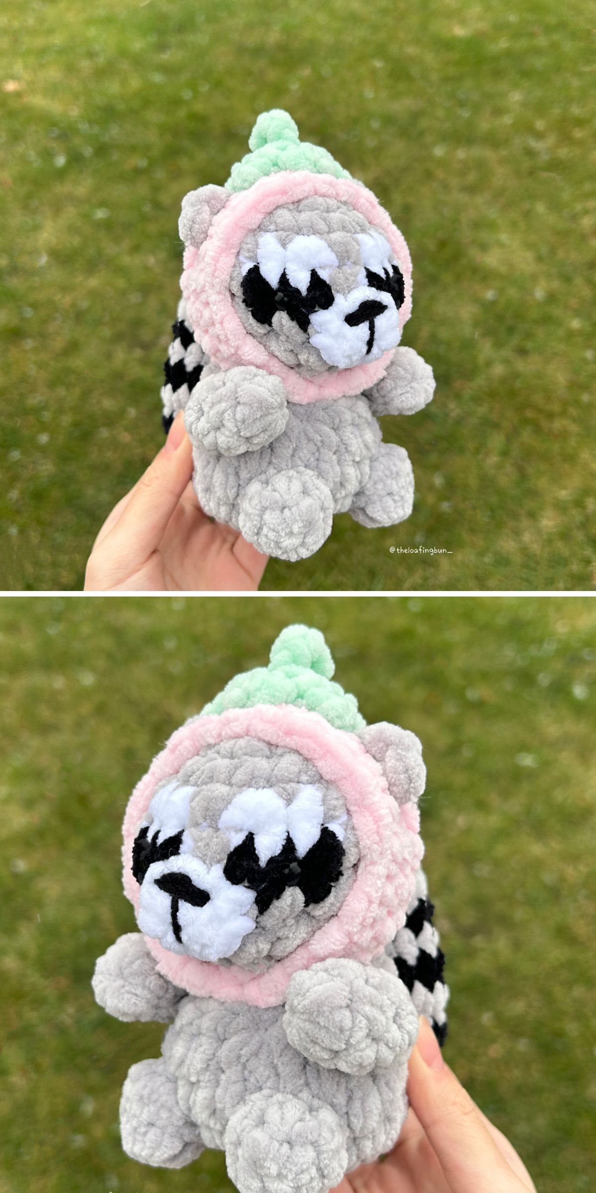 A hand holds a small, crochet raccoon plush toy with a pink and green hood outdoors over a grassy background.