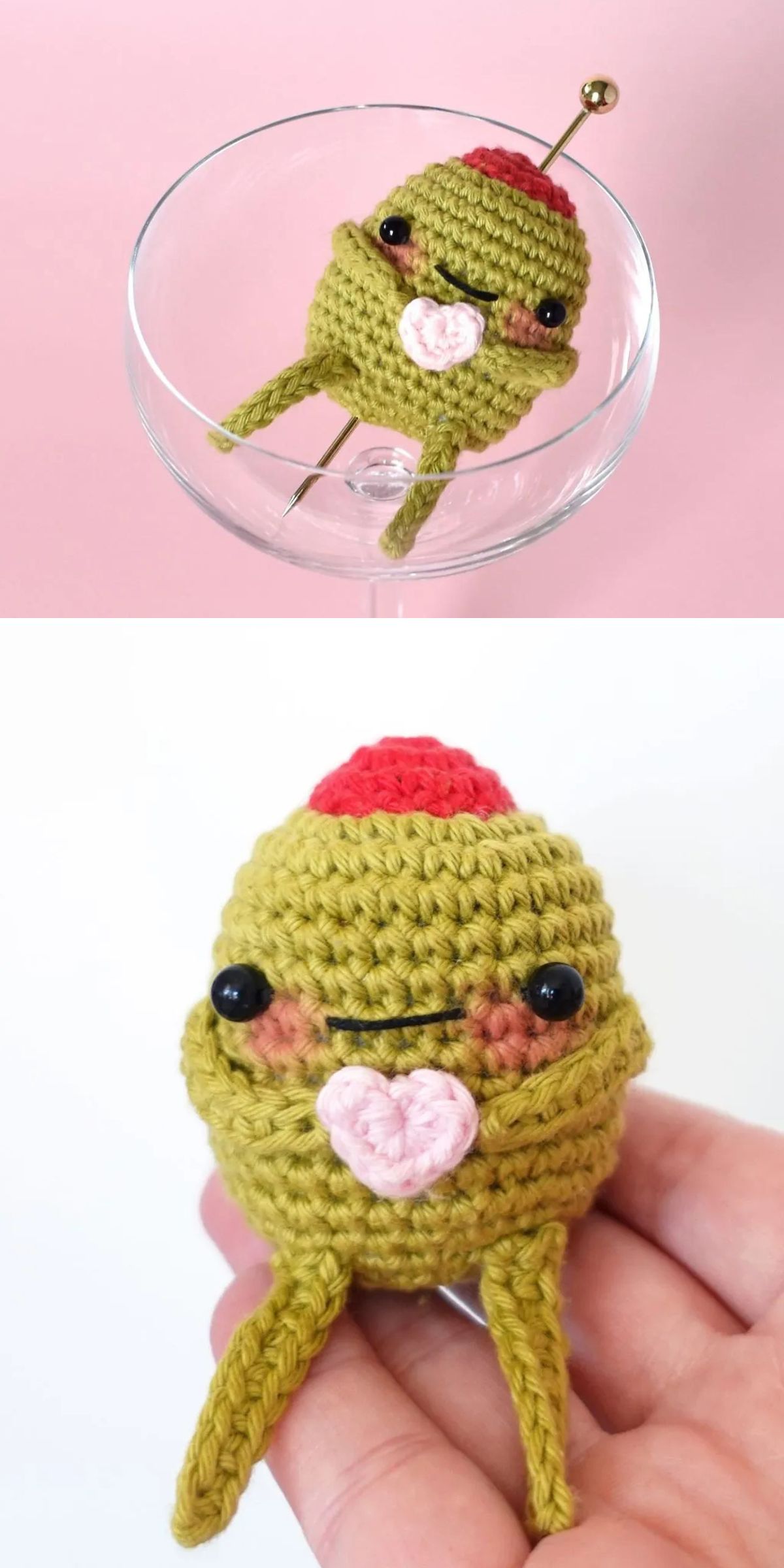 A small food amigurumi green olive with a red top, black eyes, and a smiling mouth holds a pink heart, displayed in a glass and gently held in a hand.