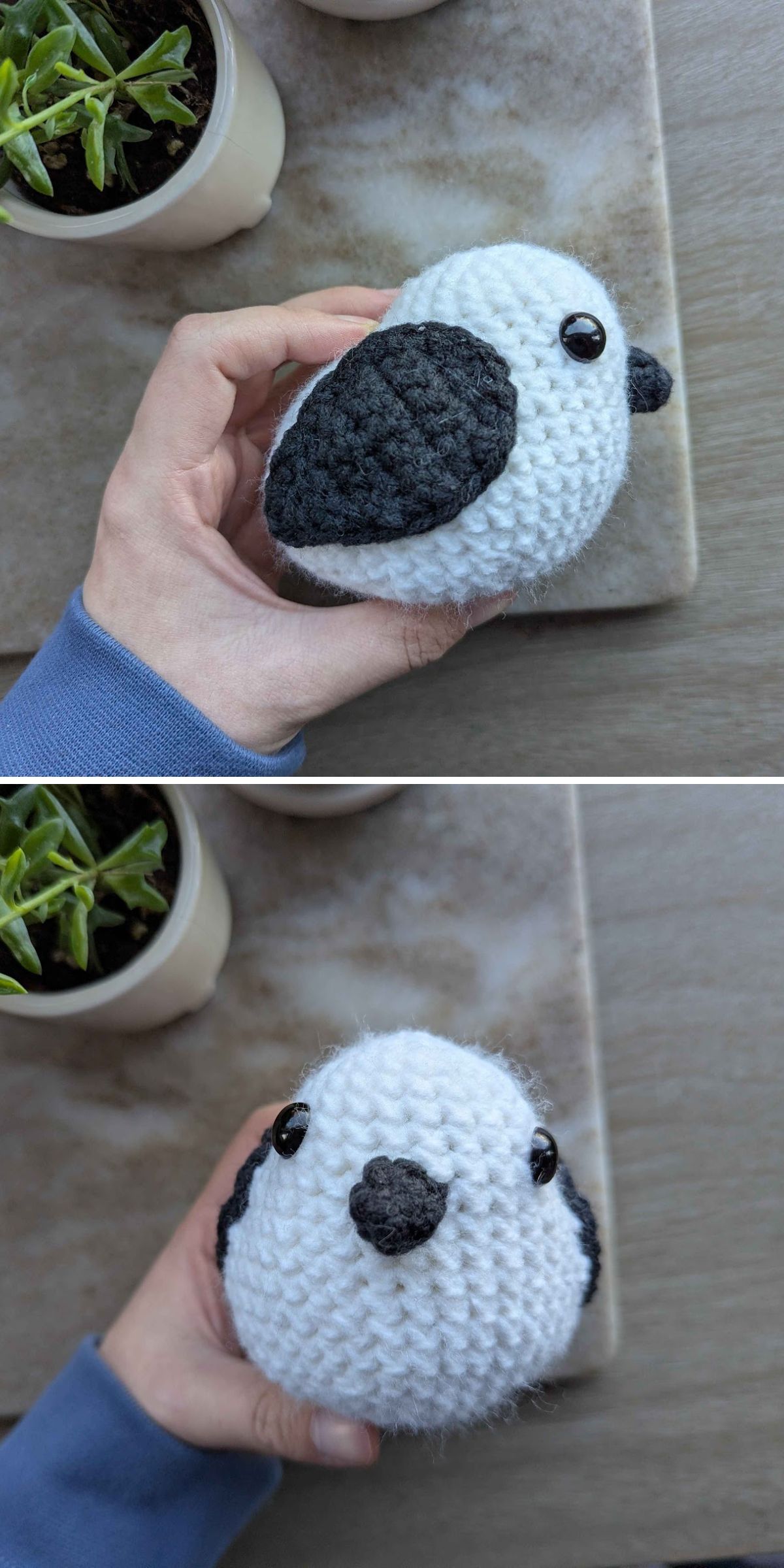 A hand holds a small crochet bird made with black and white yarn, featuring black button eyes, near two potted plants on a wooden surface.