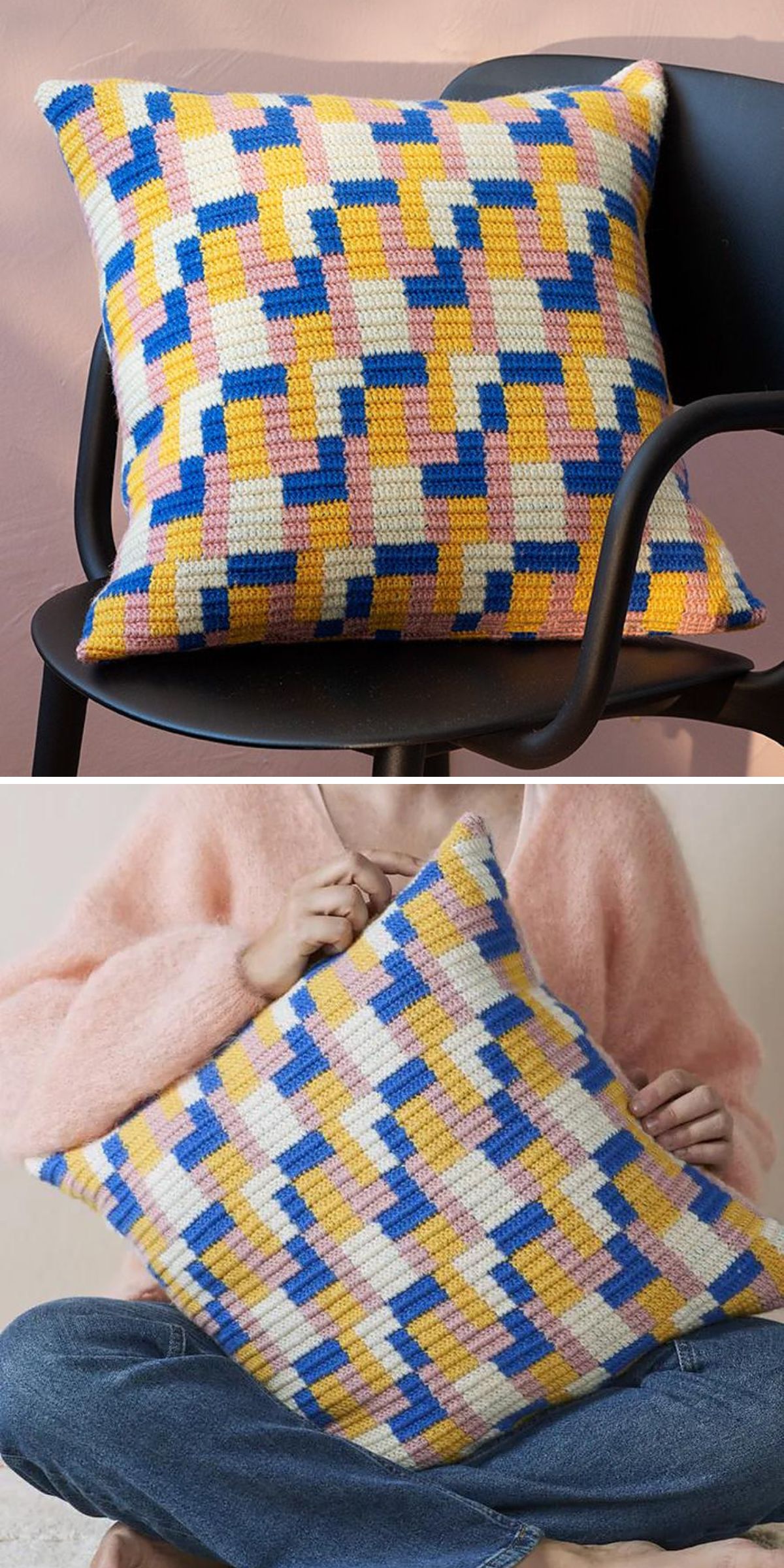 A crochet pillow with a geometric pattern in yellow, blue, pink, and white, shown on a black chair and held by a person wearing a pink sweater.