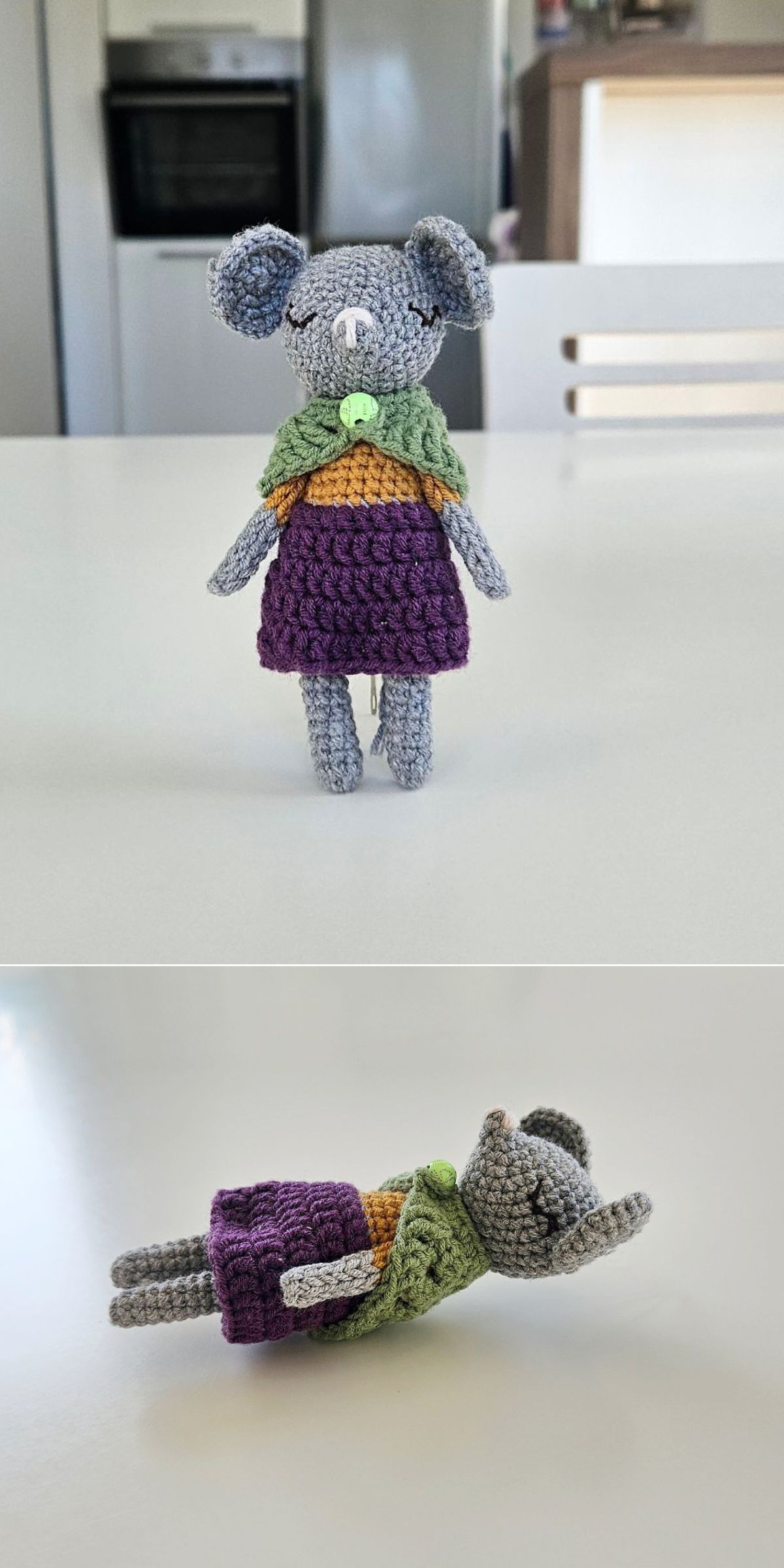 A handmade amigurumi mice doll with a purple dress and green cape is shown standing upright and lying on its back on a white surface.