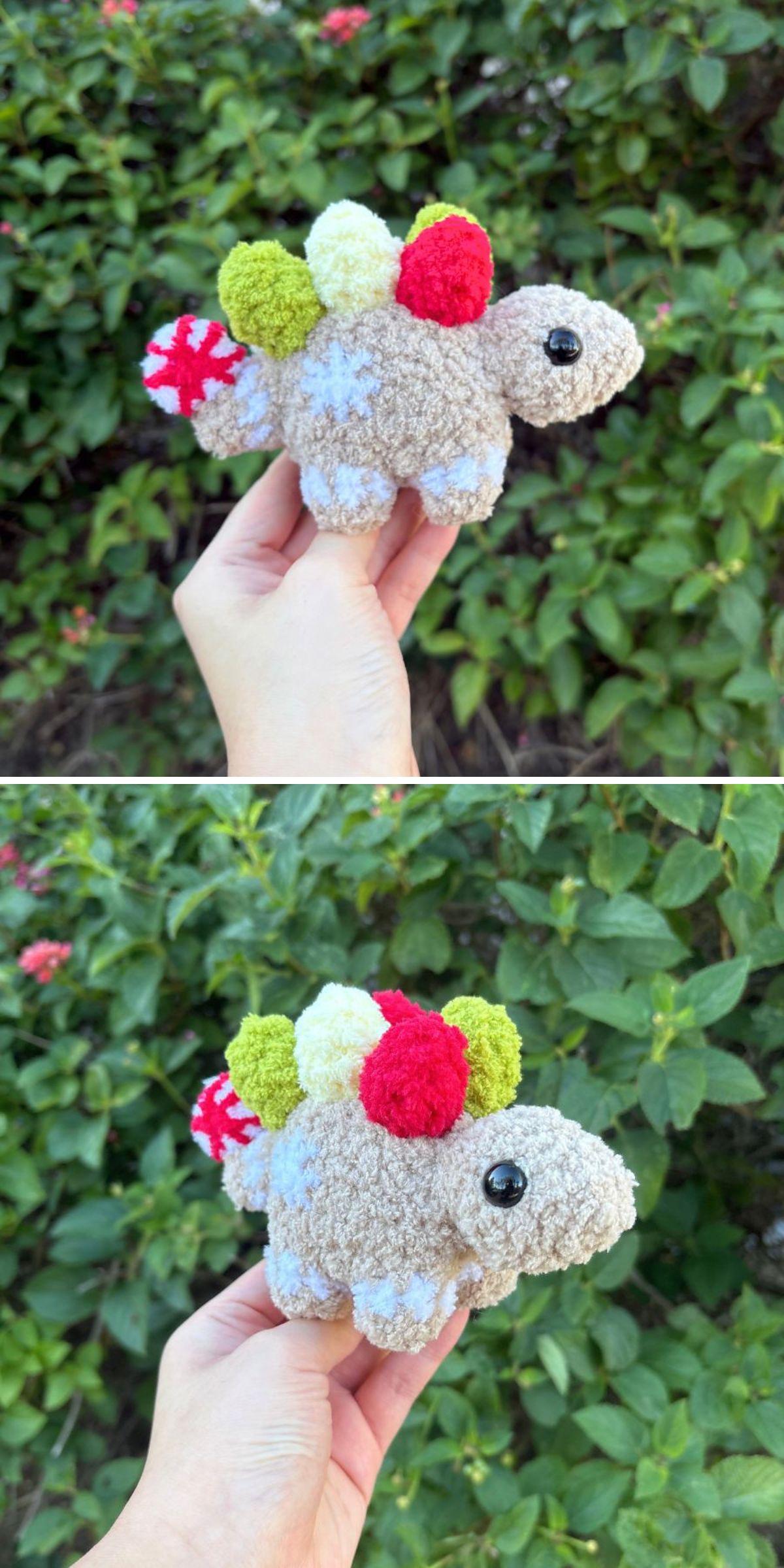 A hand holds a small, crochet dinosaur plush toy with pom-poms on its back, set against a background of green leafy bushes.