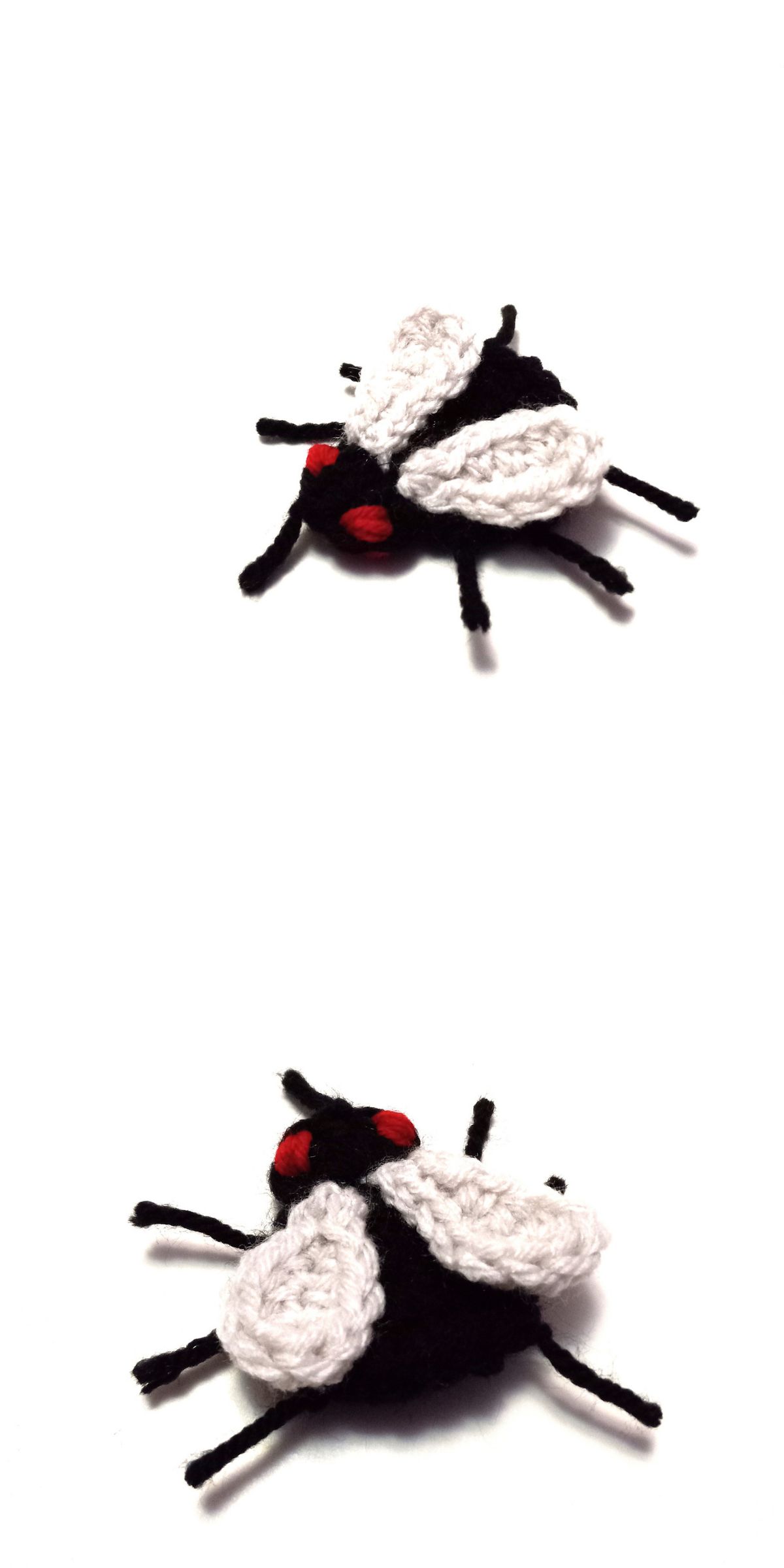 A small, black and white crocheted fly with red eyes is shown from two different angles on a white background, perfect for those seeking nature-inspired crochet ideas.
