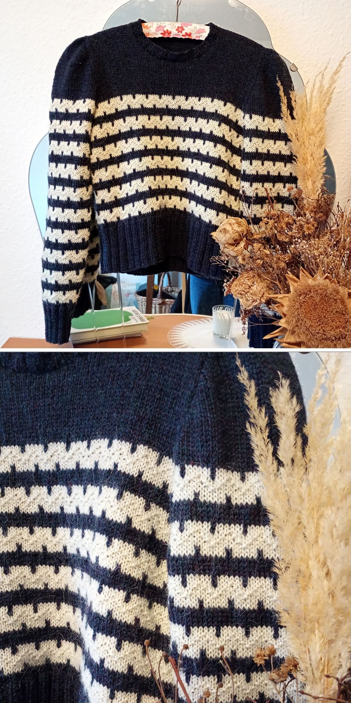 A dark blue and white striped knit sweater is displayed on a hanger above a table with dried grasses and decorative items, highlighting the cozy appeal of this classic knit sweater.