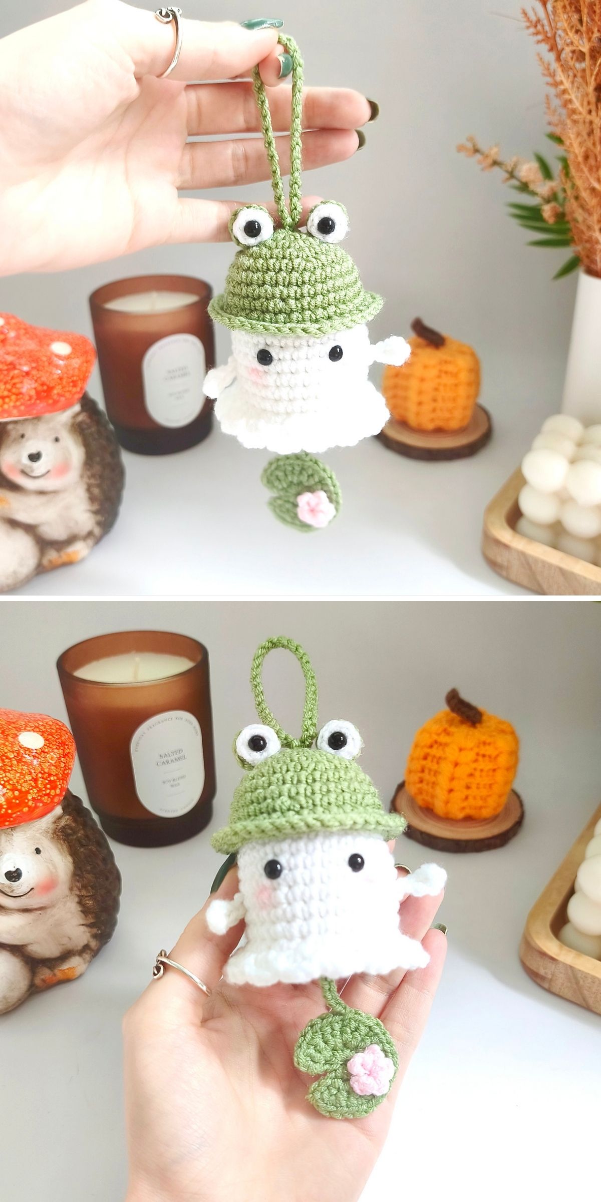 A hand holds a small crochet ghost charm shaped like a ghost wearing a green frog hat with a lily pad and flower dangling below.