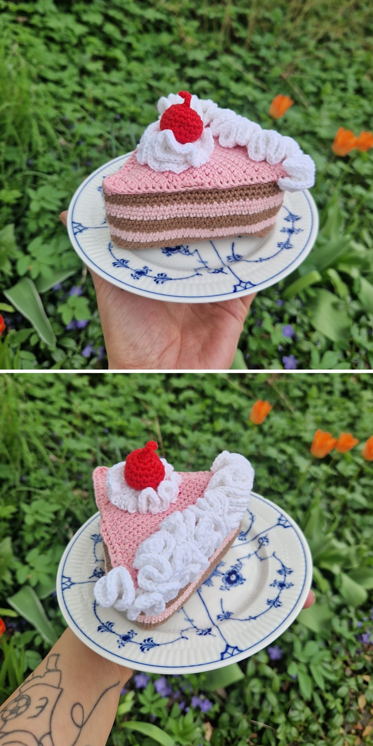 A hand holds a plate with a crochet dessert — a slice of cake topped with a red cherry — with green grass and orange flowers in the background.
